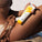 Model holding Tropic Great Barrier Sun Lotion SPF 50 while sitting on the beach, showing sun protection skincare in a summer setting.